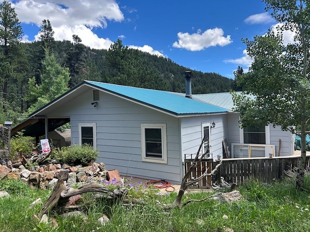 back of property with metal roof, a wooded view, and fence