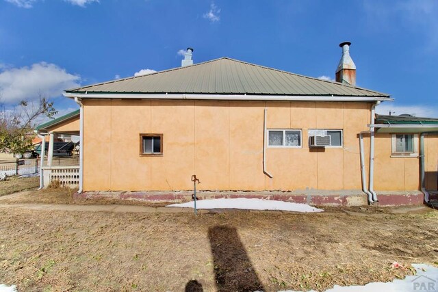 view of side of home with metal roof, a chimney, and stucco siding