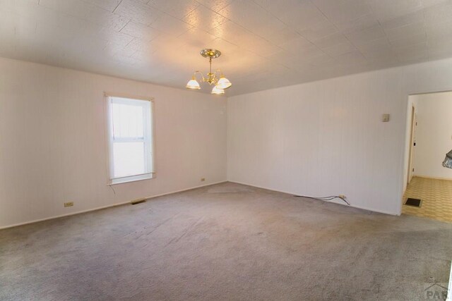 carpeted empty room featuring visible vents and a chandelier