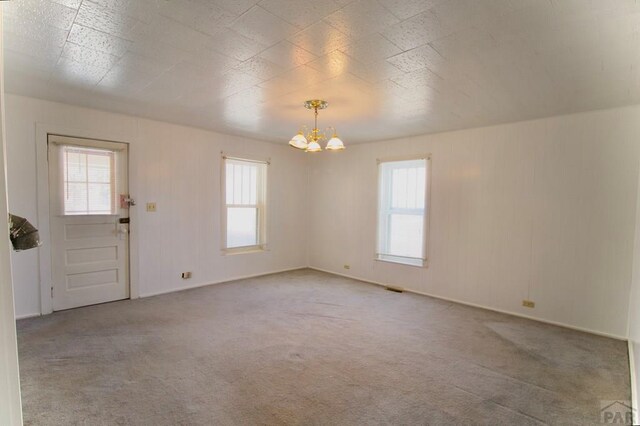 carpeted spare room featuring plenty of natural light, visible vents, and a chandelier