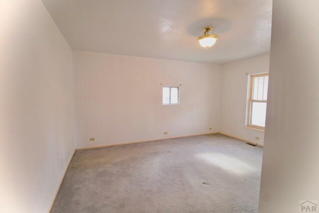 unfurnished room featuring a wealth of natural light, light colored carpet, visible vents, and baseboards