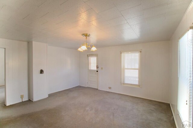 carpeted spare room featuring an inviting chandelier