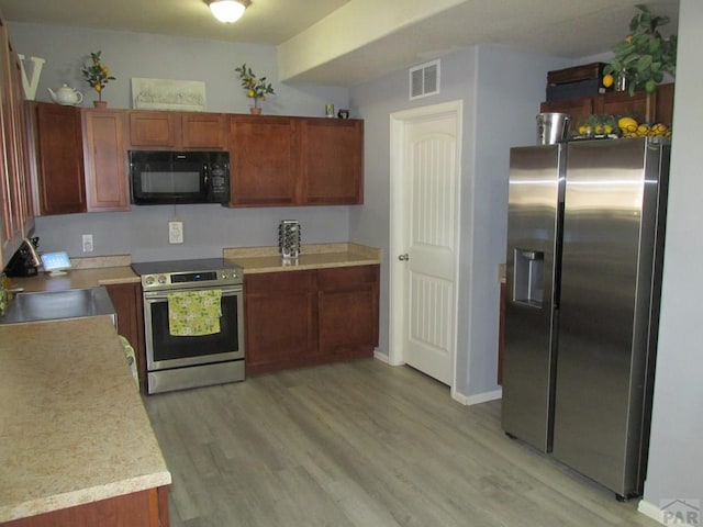 kitchen featuring a sink, visible vents, light countertops, appliances with stainless steel finishes, and light wood finished floors