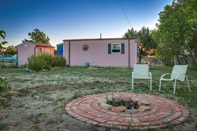 back of house with a yard, an outbuilding, fence, and a fire pit