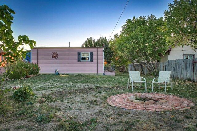 rear view of house featuring an outdoor fire pit, a lawn, and fence