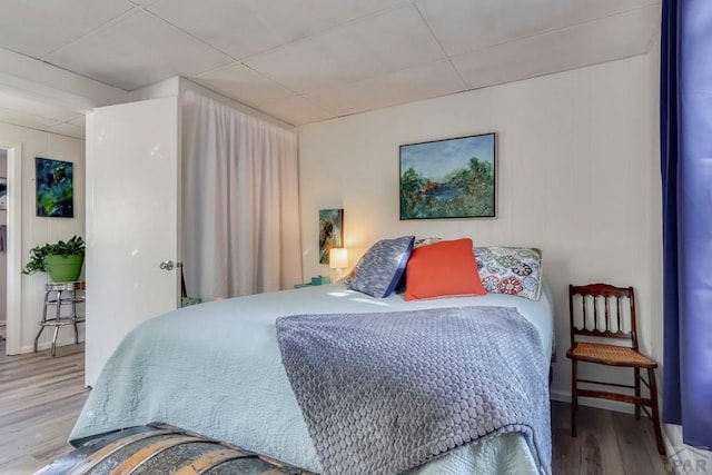 bedroom with a drop ceiling, baseboards, and wood finished floors