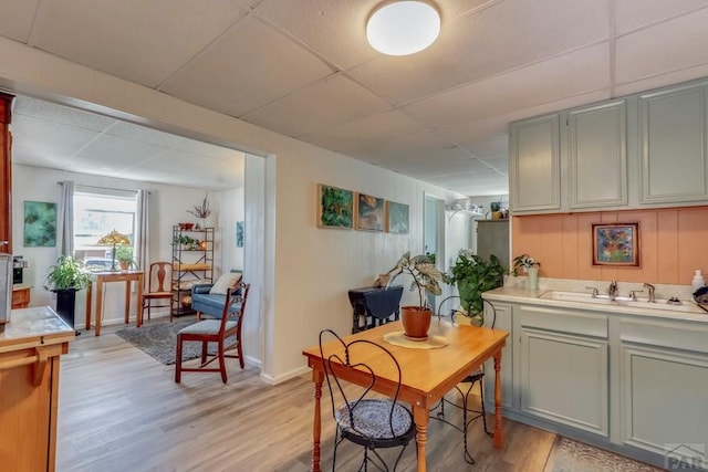 dining area featuring light wood-style floors, a drop ceiling, and baseboards