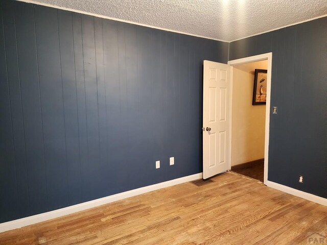 spare room with light wood-style flooring, baseboards, and a textured ceiling