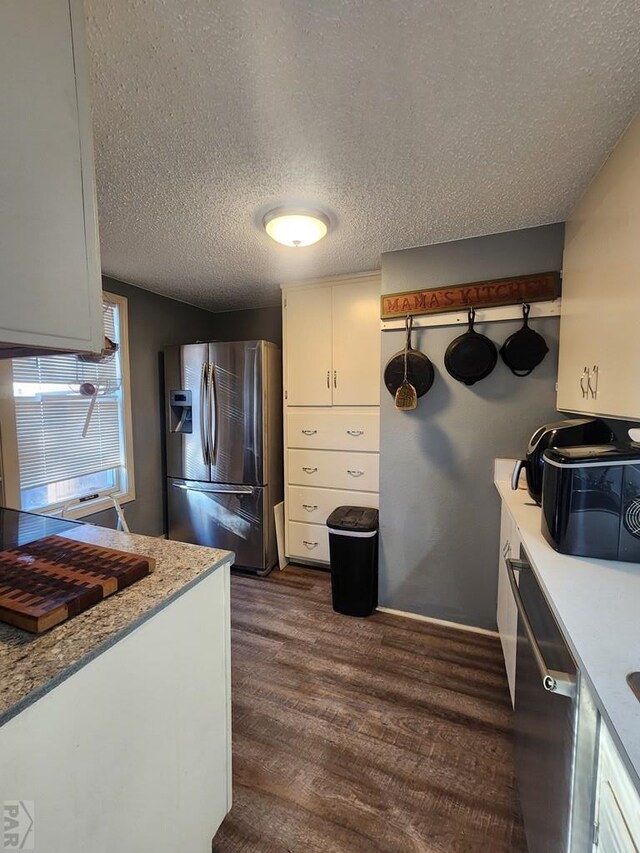 kitchen featuring dark wood-style flooring, appliances with stainless steel finishes, white cabinets, a textured ceiling, and light stone countertops