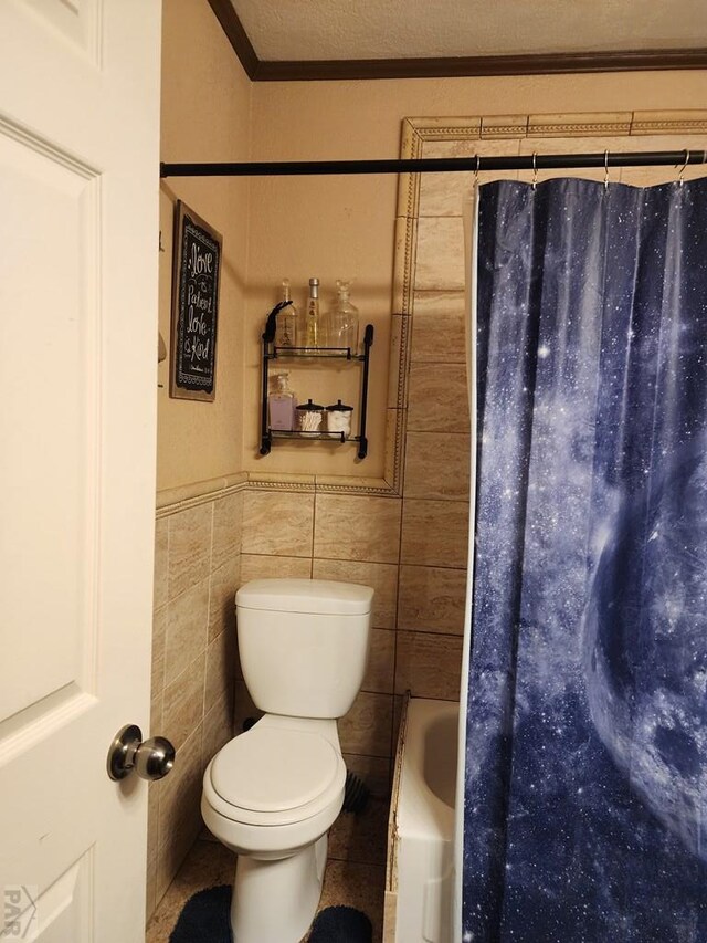 bathroom featuring a textured ceiling, toilet, a wainscoted wall, tile walls, and crown molding