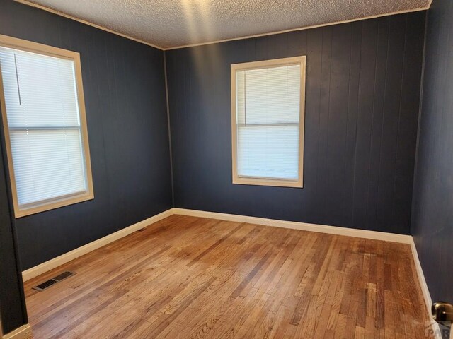 empty room with baseboards, a textured ceiling, visible vents, and wood finished floors