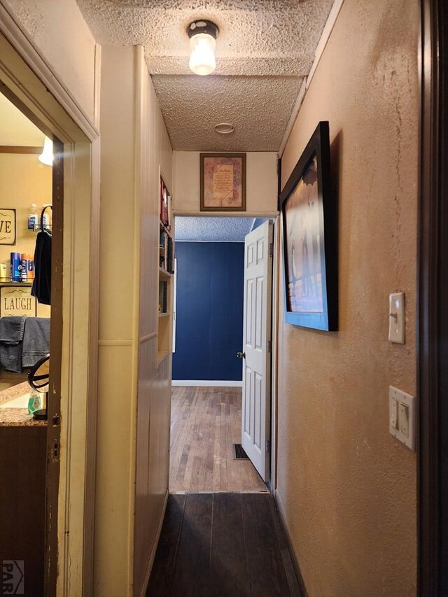 hallway with a textured ceiling, a textured wall, and dark wood-style flooring