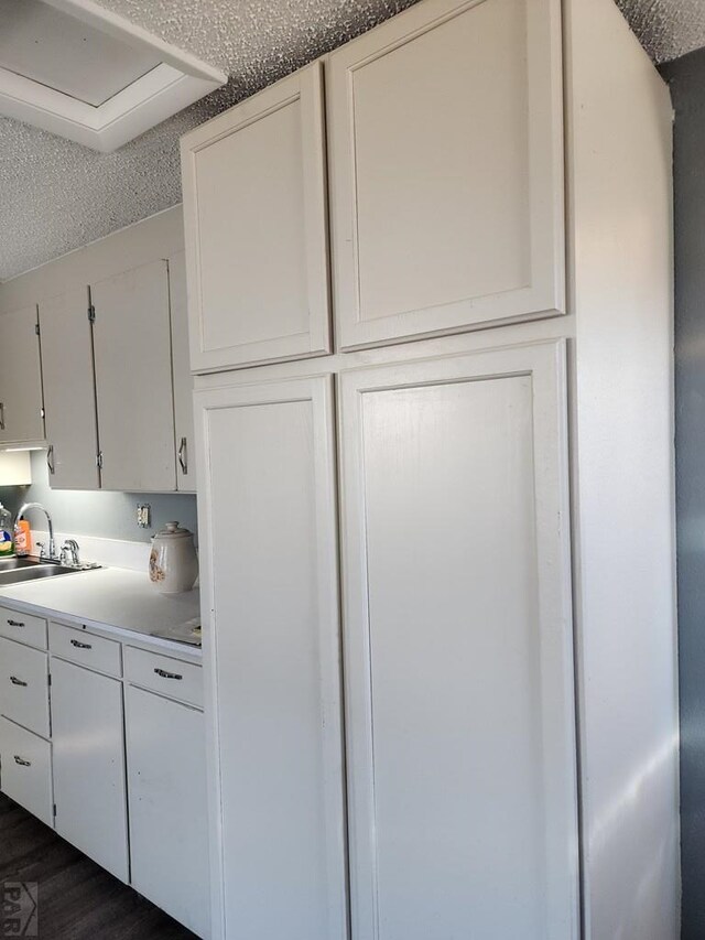 kitchen featuring a textured ceiling, a sink, white cabinetry, light countertops, and dark wood finished floors