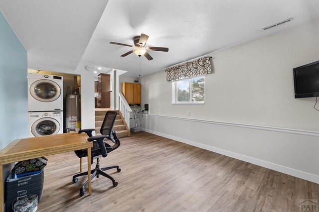 office space featuring baseboards, water heater, visible vents, and stacked washer / dryer