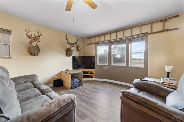 living area with a ceiling fan, light wood-style flooring, and baseboards