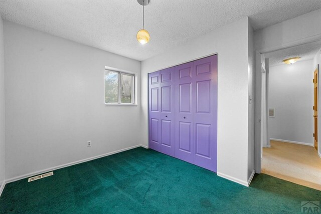 unfurnished bedroom with a closet, visible vents, dark carpet, and a textured ceiling