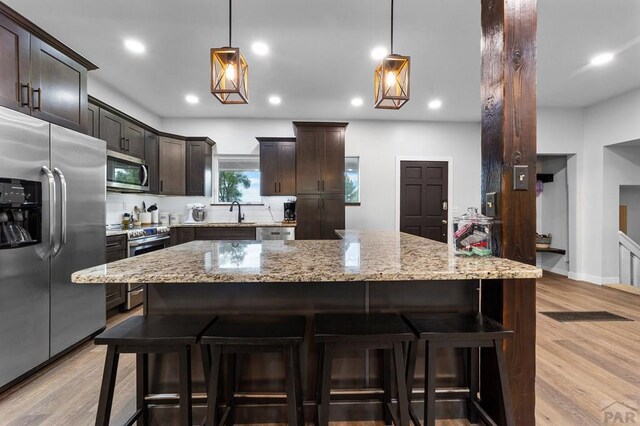 kitchen with hanging light fixtures, appliances with stainless steel finishes, light stone counters, and dark brown cabinets