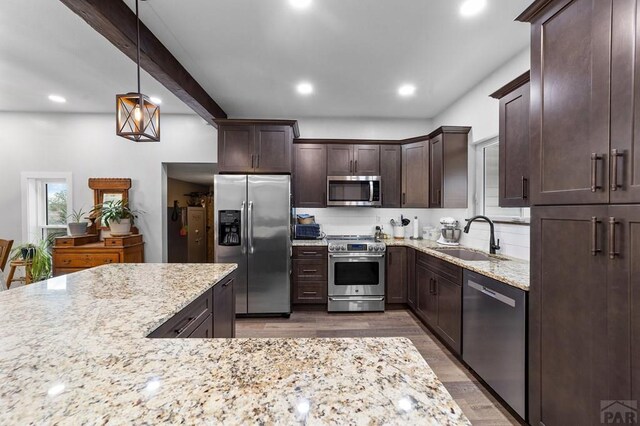 kitchen featuring stainless steel appliances, decorative light fixtures, a sink, and light stone countertops