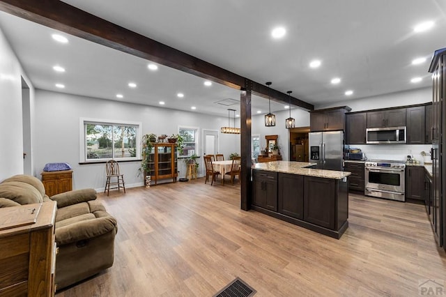 kitchen featuring light stone counters, open floor plan, appliances with stainless steel finishes, beamed ceiling, and decorative light fixtures