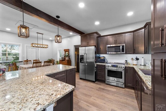 kitchen with light stone counters, decorative light fixtures, appliances with stainless steel finishes, light wood-style floors, and beamed ceiling