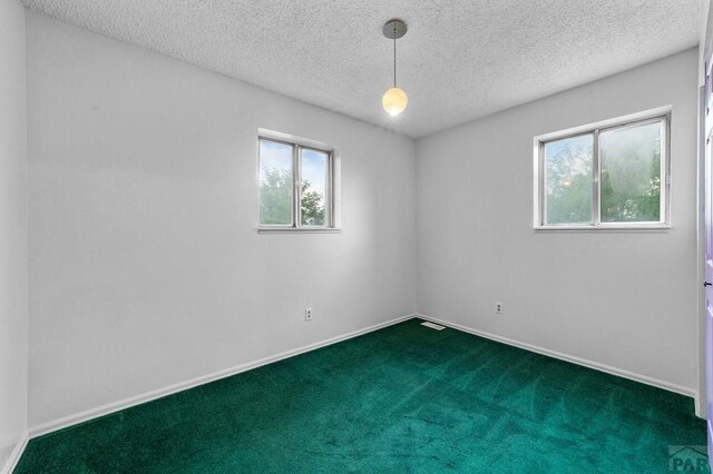 spare room featuring a healthy amount of sunlight, baseboards, dark carpet, and a textured ceiling