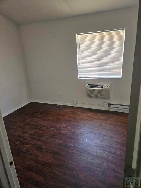 empty room featuring a wall unit AC, a baseboard heating unit, baseboards, and dark wood-type flooring