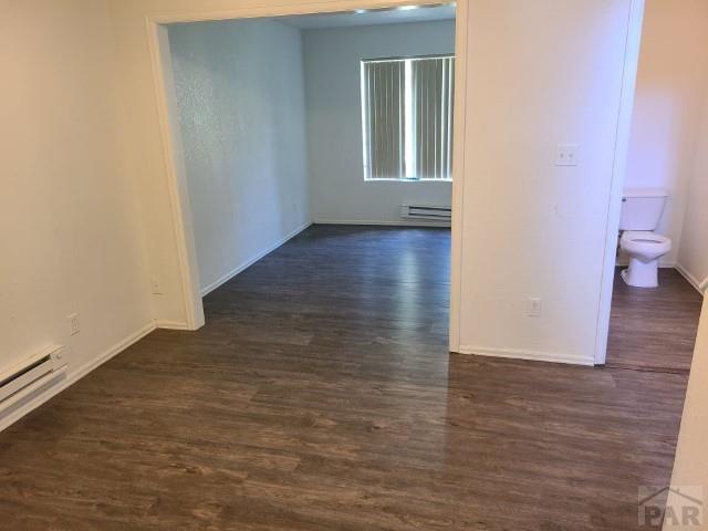 spare room featuring a baseboard heating unit, baseboards, baseboard heating, and dark wood-style flooring