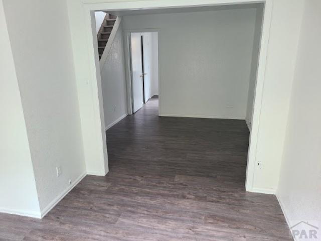 corridor with dark wood-type flooring, stairway, and baseboards