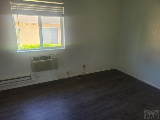 empty room featuring baseboards, a baseboard heating unit, dark wood finished floors, and an AC wall unit