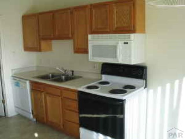 kitchen with brown cabinets, white appliances, light countertops, and a sink