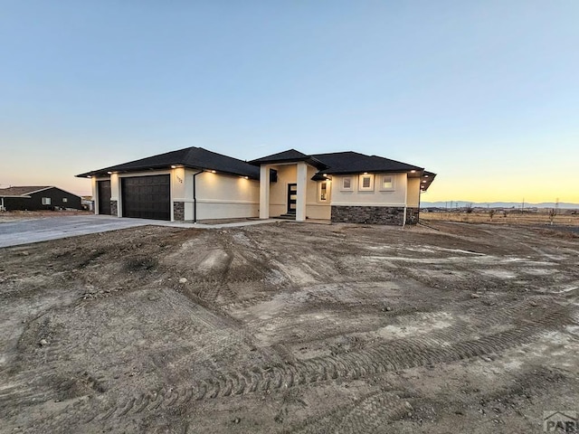 view of front of house featuring stone siding, an attached garage, concrete driveway, and stucco siding