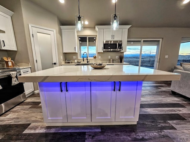 kitchen featuring light stone counters, stainless steel appliances, white cabinets, a center island, and decorative light fixtures