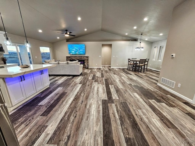 living area with lofted ceiling, ceiling fan, a fireplace, visible vents, and dark wood finished floors