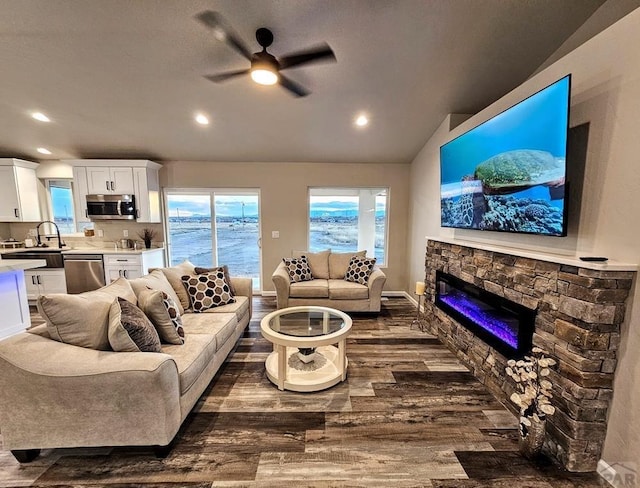 living area featuring dark wood-style floors, ceiling fan, vaulted ceiling, a stone fireplace, and recessed lighting