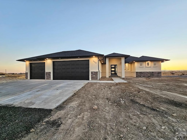 prairie-style house featuring stone siding, an attached garage, and stucco siding