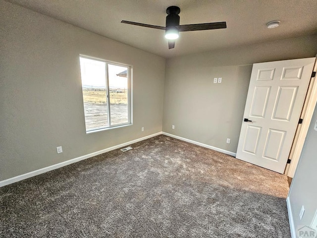 spare room with a ceiling fan, visible vents, dark carpet, and baseboards