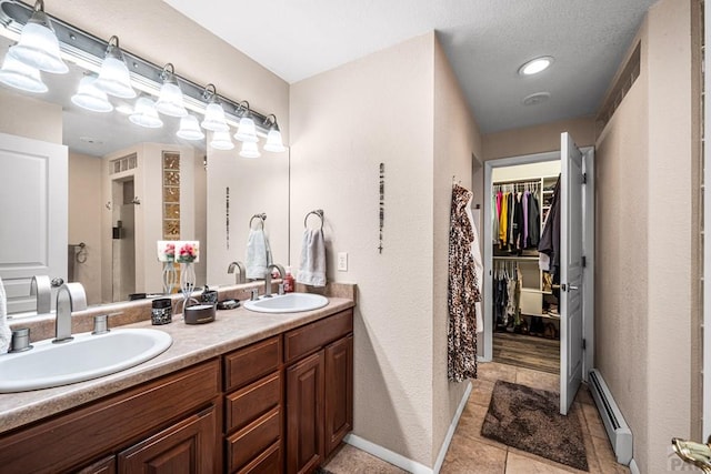 67 Macarthur Rd, Pueblo, CO 81001 - bathroom featuring double vanity, a baseboard heating unit, tile patterned flooring, a walk in closet, and a textured wall