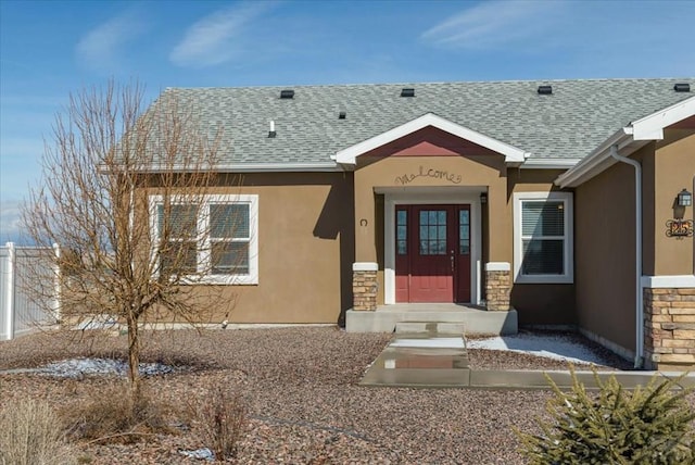 property entrance with stone siding, roof with shingles, and stucco siding