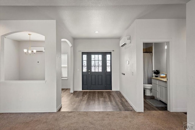 entryway featuring a textured ceiling, dark carpet, arched walkways, and a wall mounted air conditioner