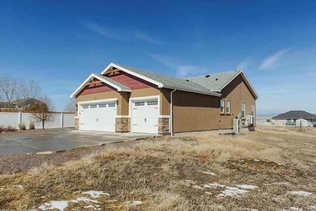 view of home's exterior featuring an attached garage, fence, stone siding, driveway, and stucco siding