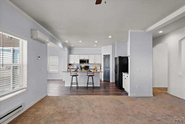 kitchen with a breakfast bar, stainless steel microwave, a wall mounted AC, a baseboard heating unit, and white cabinetry