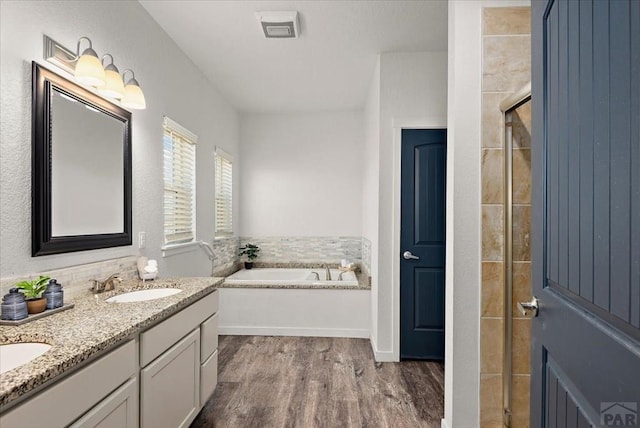 bathroom with a sink, visible vents, wood finished floors, a bath, and double vanity