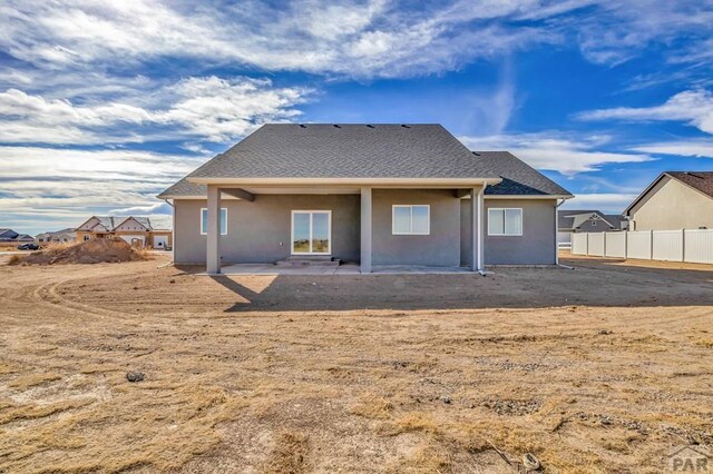 rear view of property with a patio area, roof with shingles, fence, and stucco siding