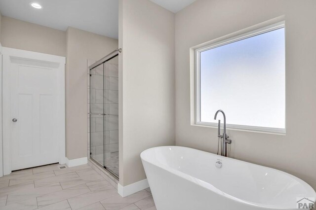 full bathroom featuring a stall shower, marble finish floor, a freestanding bath, and baseboards