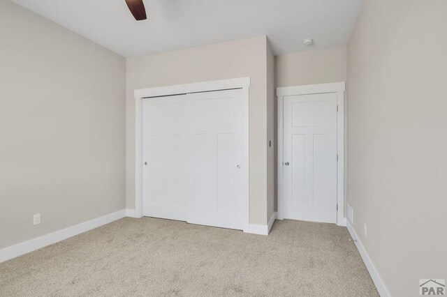 unfurnished bedroom featuring a closet, light carpet, ceiling fan, and baseboards