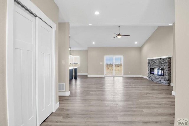 unfurnished living room featuring light wood finished floors, visible vents, a ceiling fan, vaulted ceiling, and a fireplace