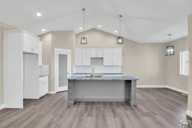 kitchen with a sink, white cabinetry, light stone countertops, an island with sink, and pendant lighting