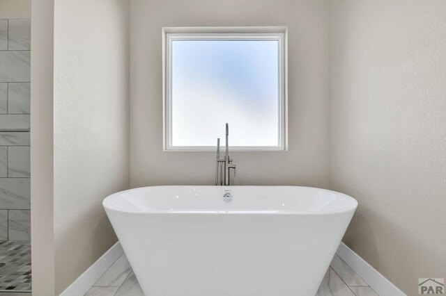 bathroom featuring a freestanding tub, baseboards, and marble finish floor