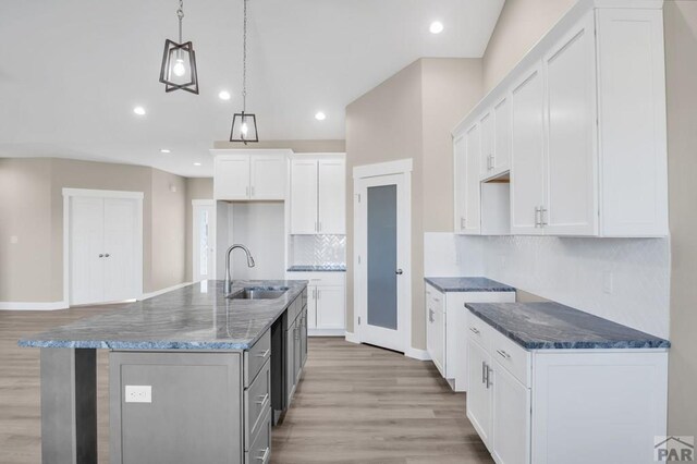 kitchen with a sink, white cabinets, an island with sink, dark stone countertops, and decorative light fixtures