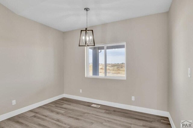 empty room with visible vents, baseboards, a chandelier, and wood finished floors